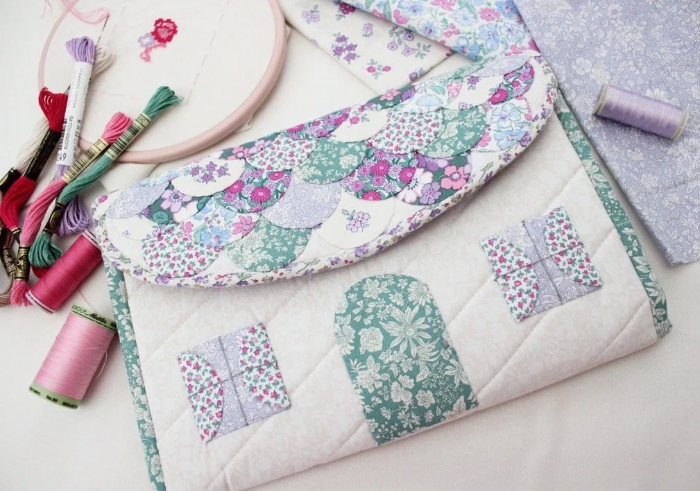 A quilting project in progress with a partially finished quilt, sewing threads, and embroidery floss on a white surface.