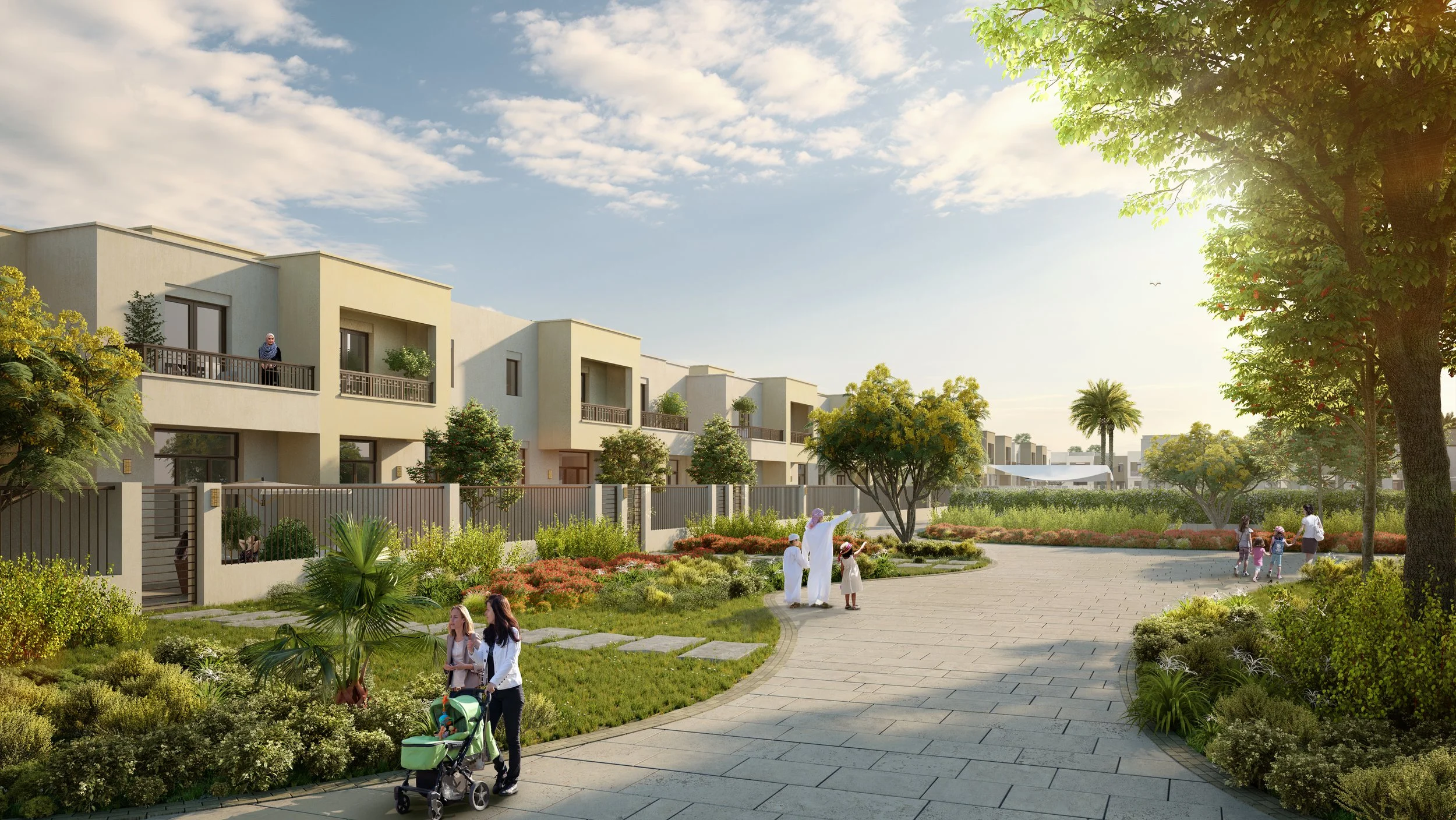 A modern residential neighborhood with row houses, green lawns, trees, and walking paths. People, including families with children, are enjoying outdoor activities in the sunny, landscaped area.