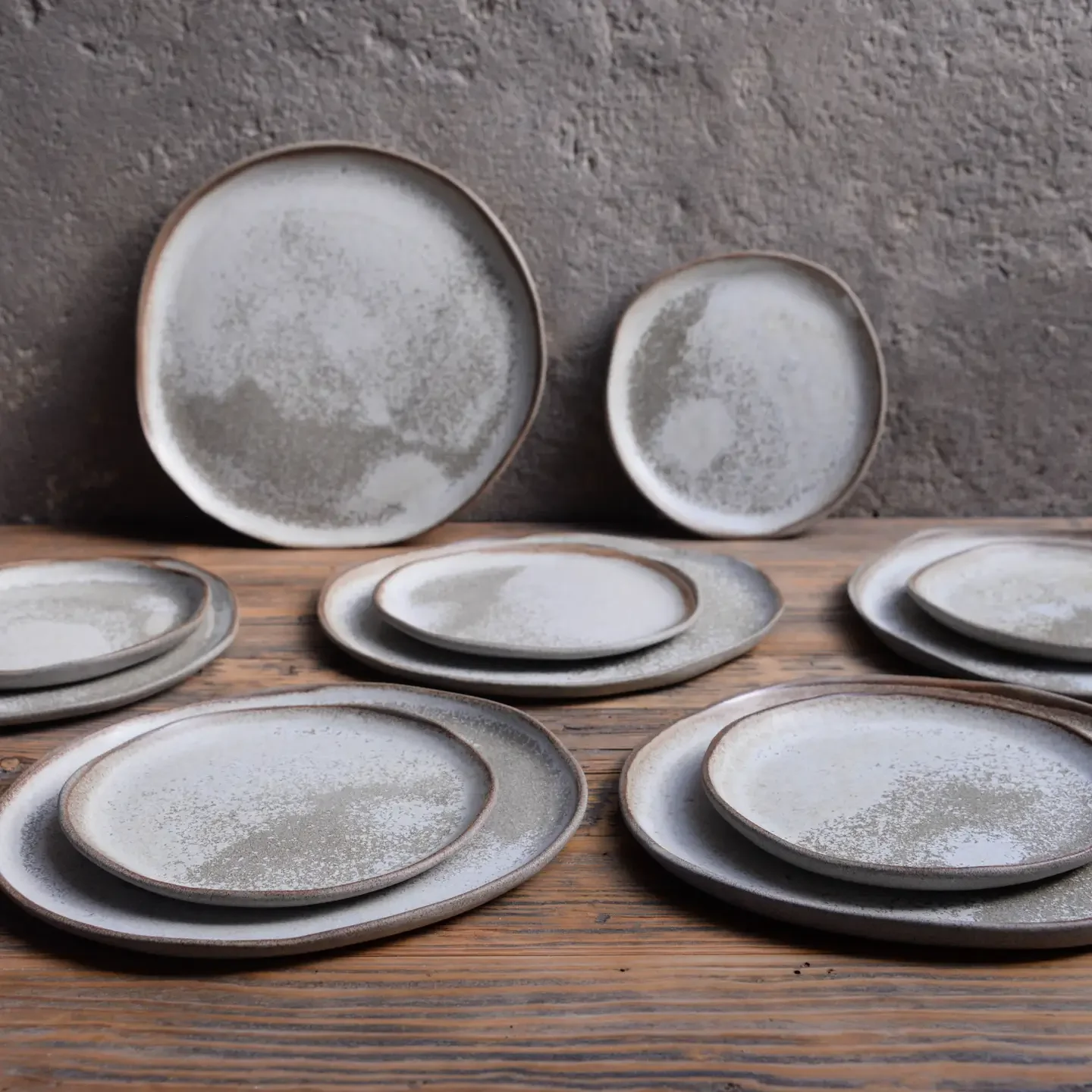 A collection of ceramic plates and bowls with a speckled gray and white design, arranged on a wooden surface against a textured gray wall.