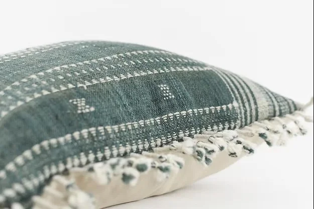 Close-up of a decorative cushion with a green and white woven pattern and fringed edges.