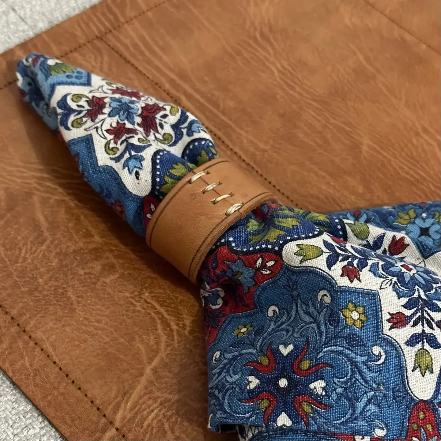 A knife with a handle that resembles a folded bandana in red, white, blue, green, and yellow floral pattern, resting on a brown leather surface.