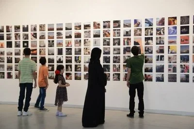 People viewing a large wall display of numerous photographs at an art gallery