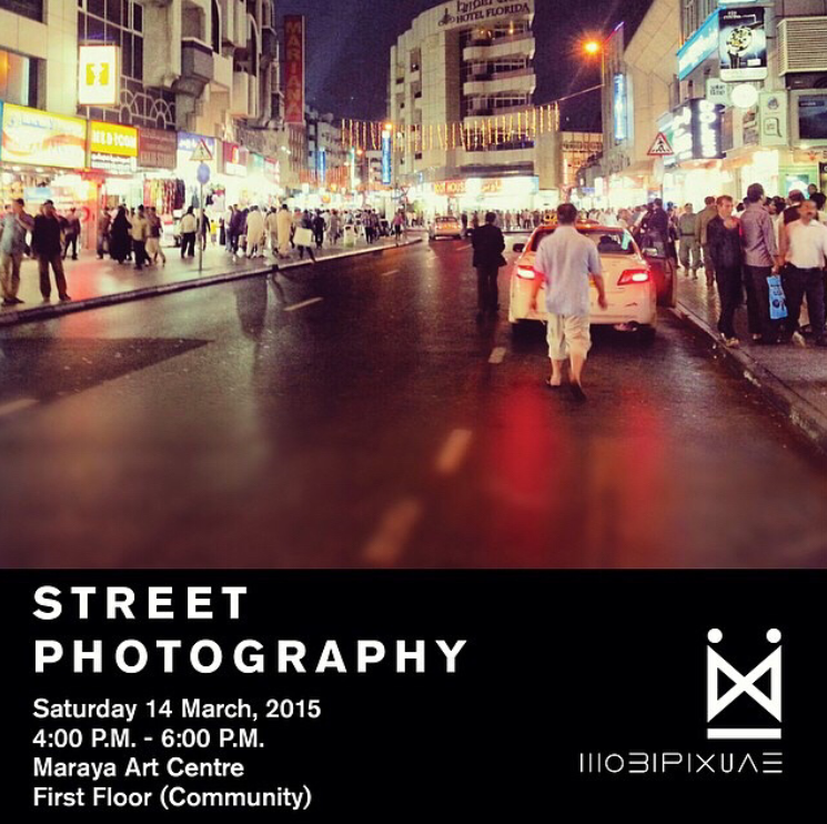 A night scene of a busy city street with many pedestrians walking on the sidewalks, cars parked along the curb, and bright lights from shops and signs illuminating the street. The image is used as a promotional flyer for a street photography event.
