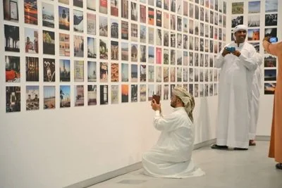 People in traditional Middle Eastern clothing viewing photographs displayed on a gallery wall.