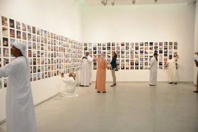People in traditional and modern clothing viewing a wall filled with photographs in an art gallery.