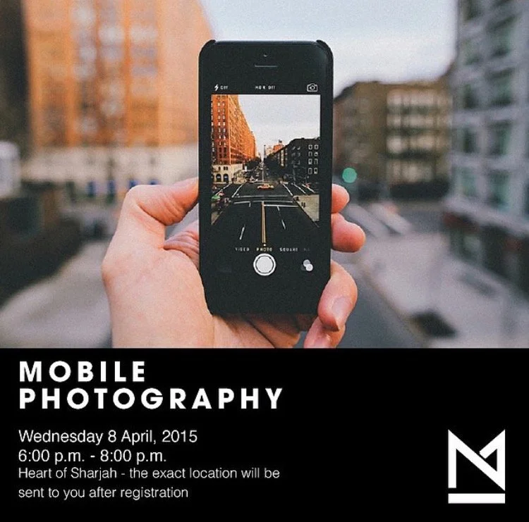 Hand holding a smartphone capturing a street scene with buildings, and a crosswalk in an urban area.