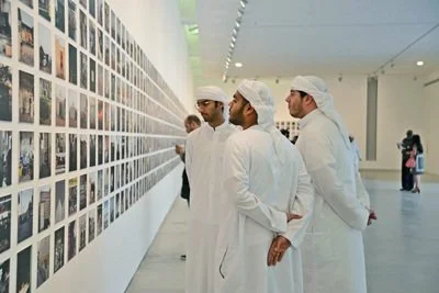 Men in white lab coats and caps examining photographs on a gallery wall.