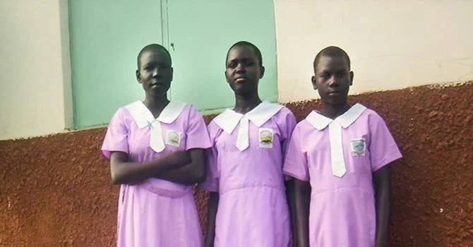 Three schoolgirls in pink uniforms with white collars standing against a wall.