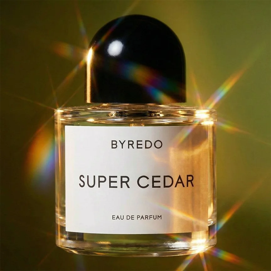A bottle of BYREDO Super Cedar Eau de Parfum with a black cap, illuminated with colorful light reflections.