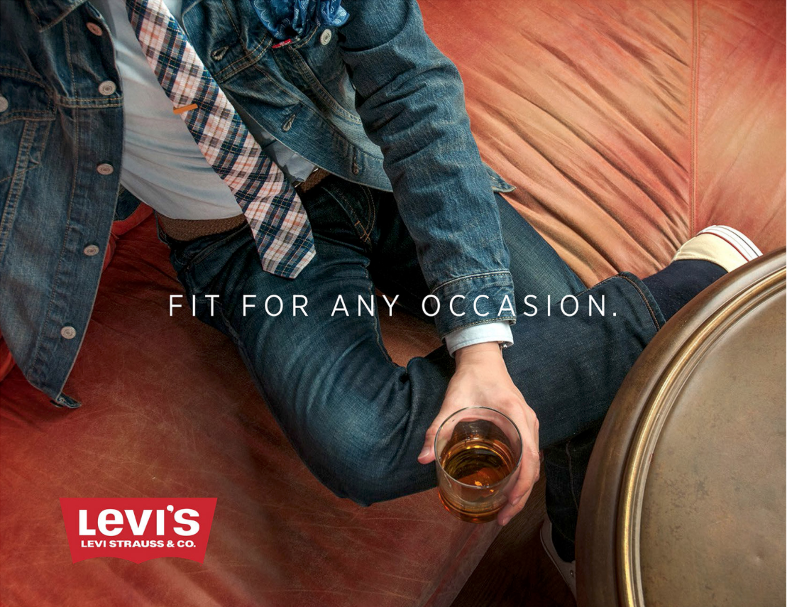 A person sitting on a leather couch, holding a glass of beer, wearing a denim jacket, plaid shirt, dark jeans, and running shoes, with the text 'Fit for any occasion' and the Levi's logo.