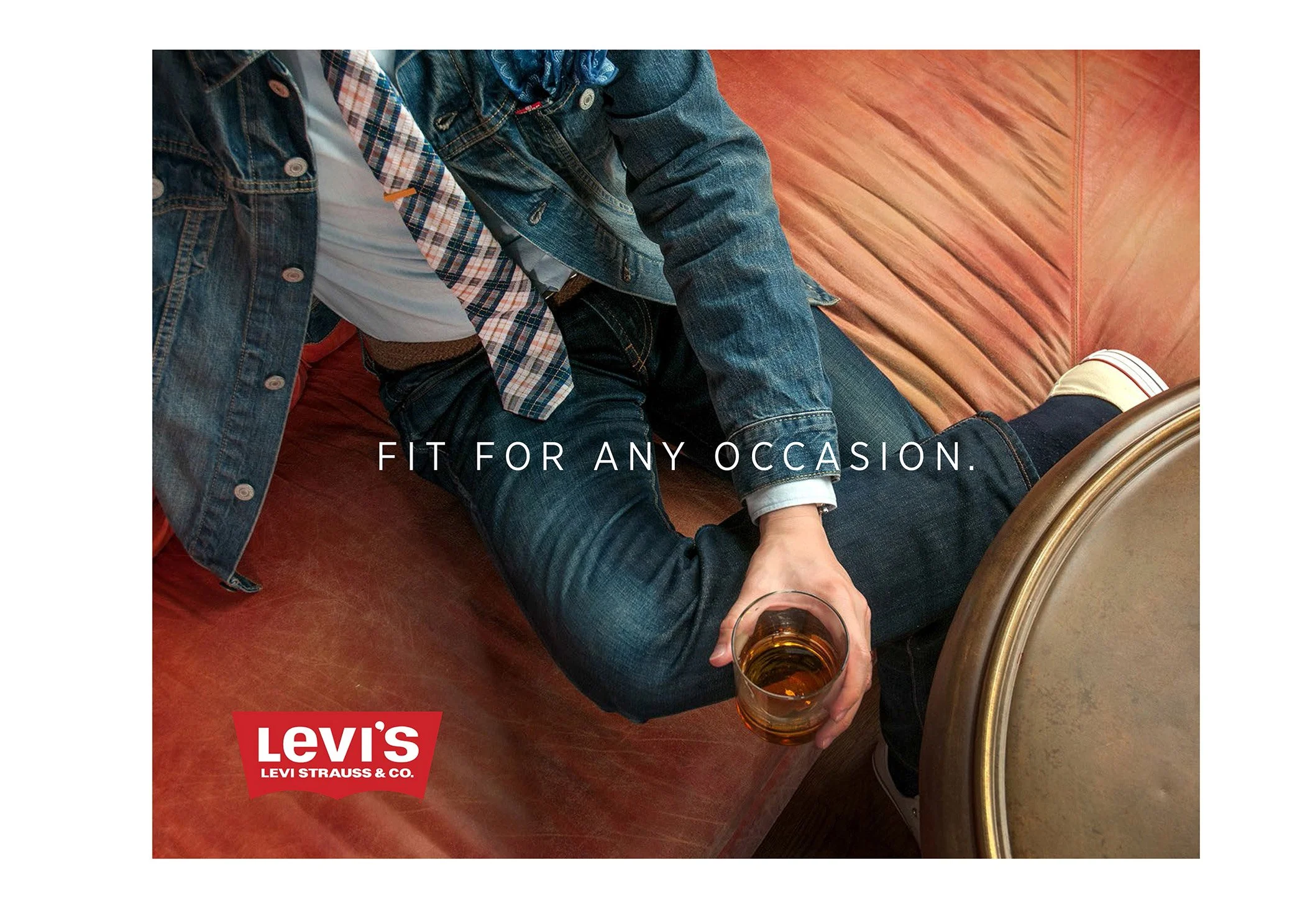 A person wearing Levi's jeans and denim jacket sitting on a leather couch, holding a glass of beer, with the text "Fit for any occasion" and Levi's logo.