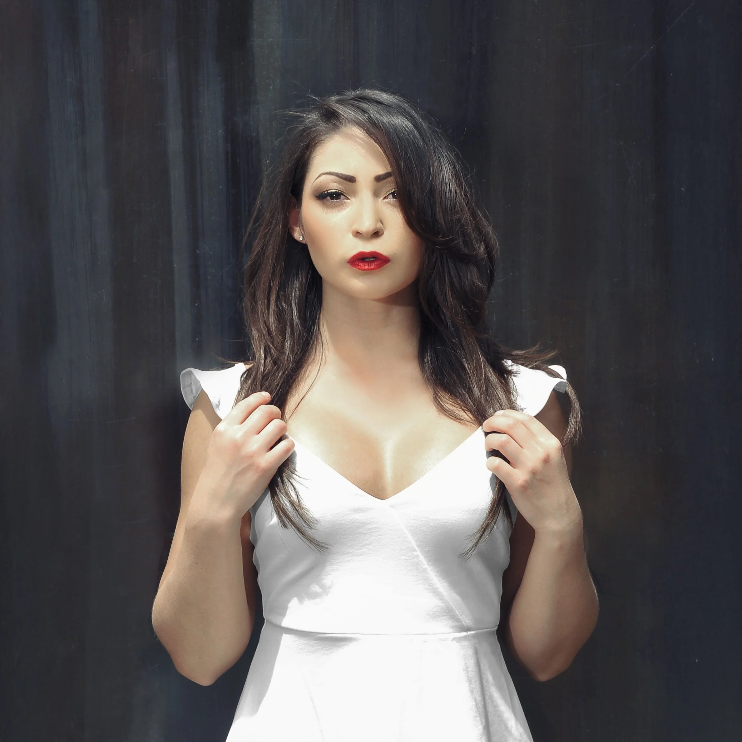 A woman with dark hair wearing a white dress against a dark background.