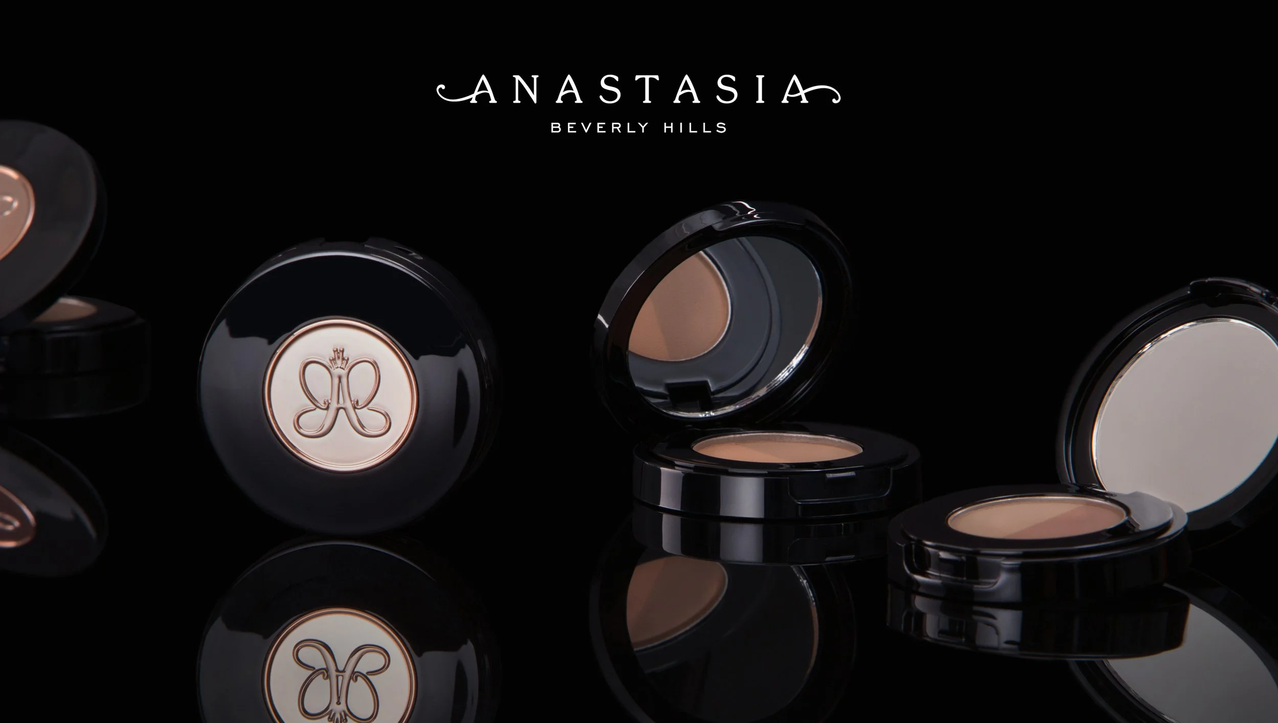 Open makeup compacts with beige foundation, displayed on a black reflective surface with the text "Anastasia Beverly Hills" at the top.