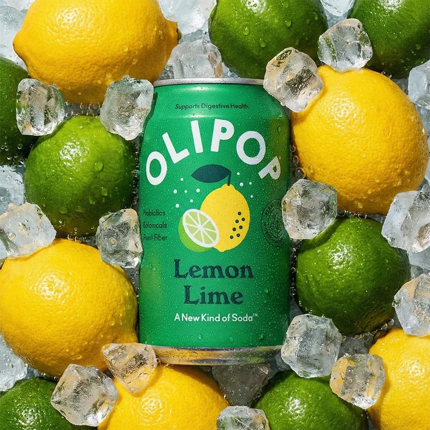 A can of Olipop Lemon Lime soda surrounded by lemons, limes, ice cubes, and water droplets.