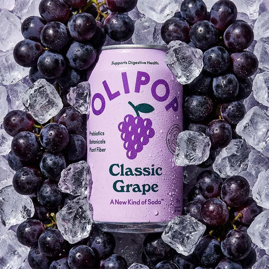 A can of Olipop Classic Grape soda surrounded by ice cubes and black grapes.