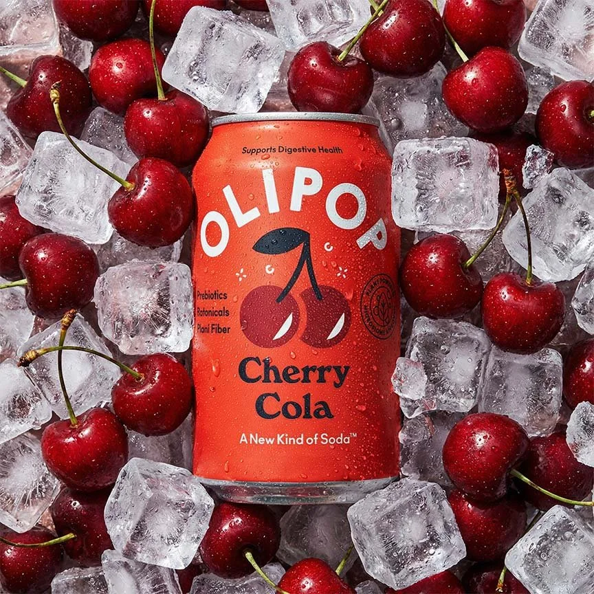 A can of Olipop Cherry Cola surrounded by ice cubes and fresh cherries.