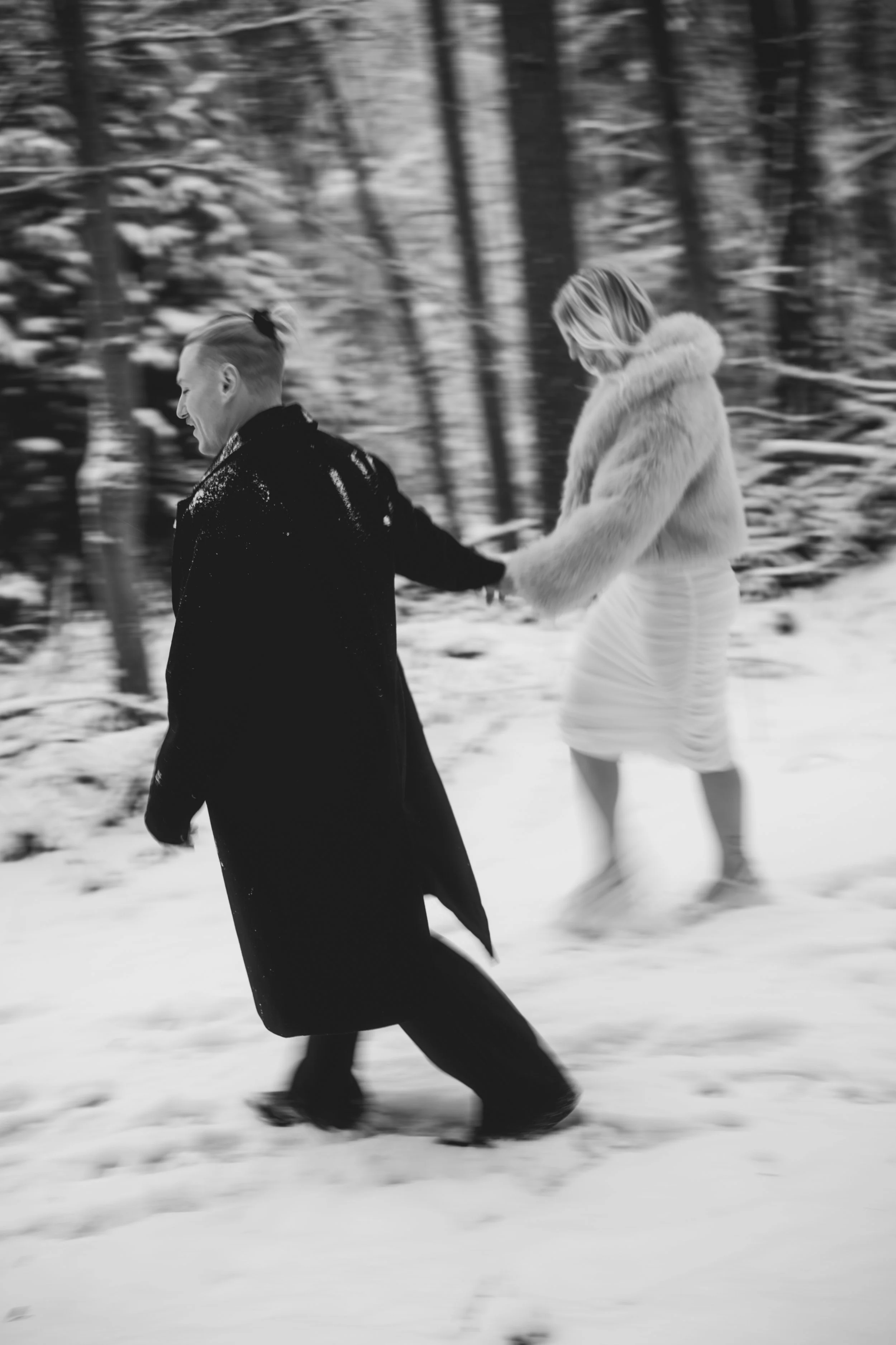 Ein Paar läuft Hand in Hand durch einen verschneiten Wald, das Bild ist schwarz-weiß.