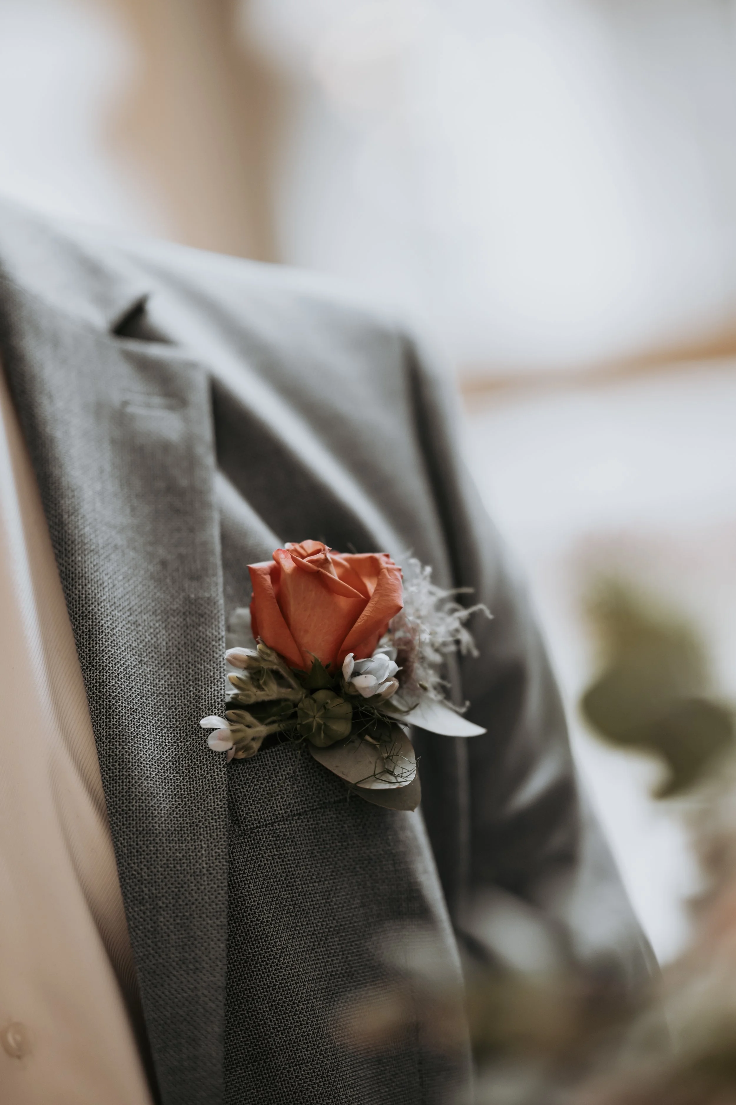 Ein graues Sakko mit einem braunen Rosenanstecker an der Brusttasche.