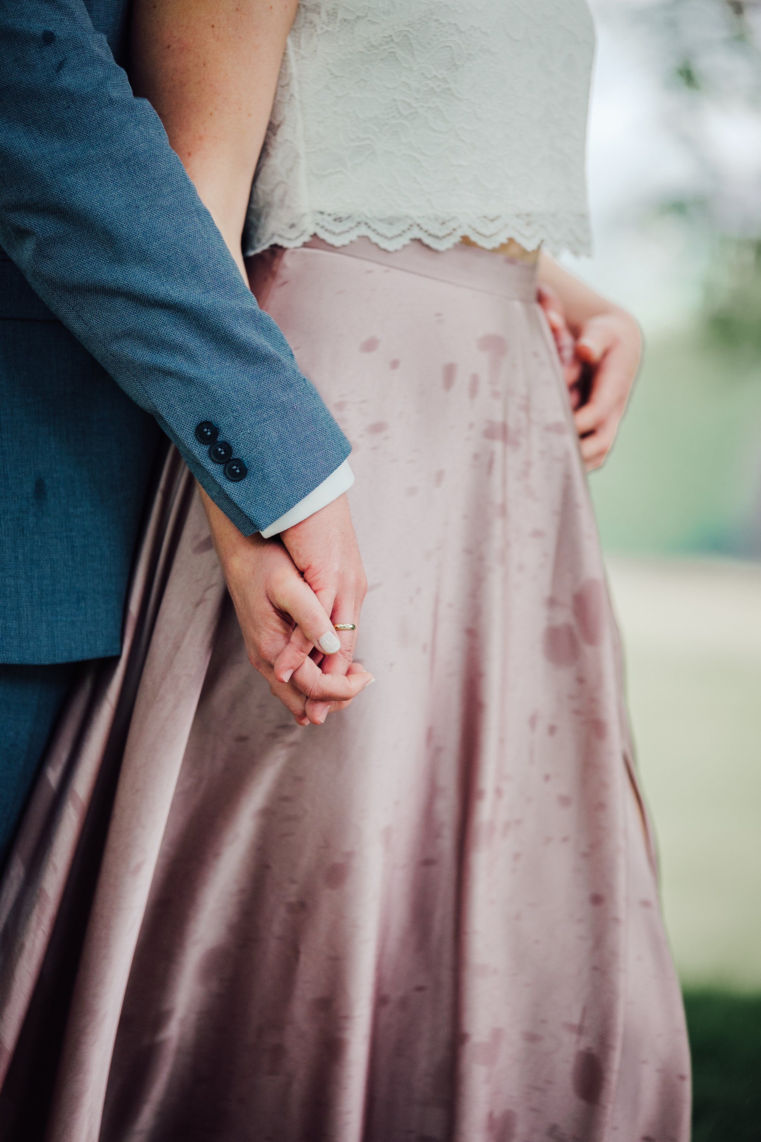 Ein Paar hält sich an den Händen bei einer Hochzeit, die Frau trägt ein rosa Kleid und der Mann einen blauen Anzug.