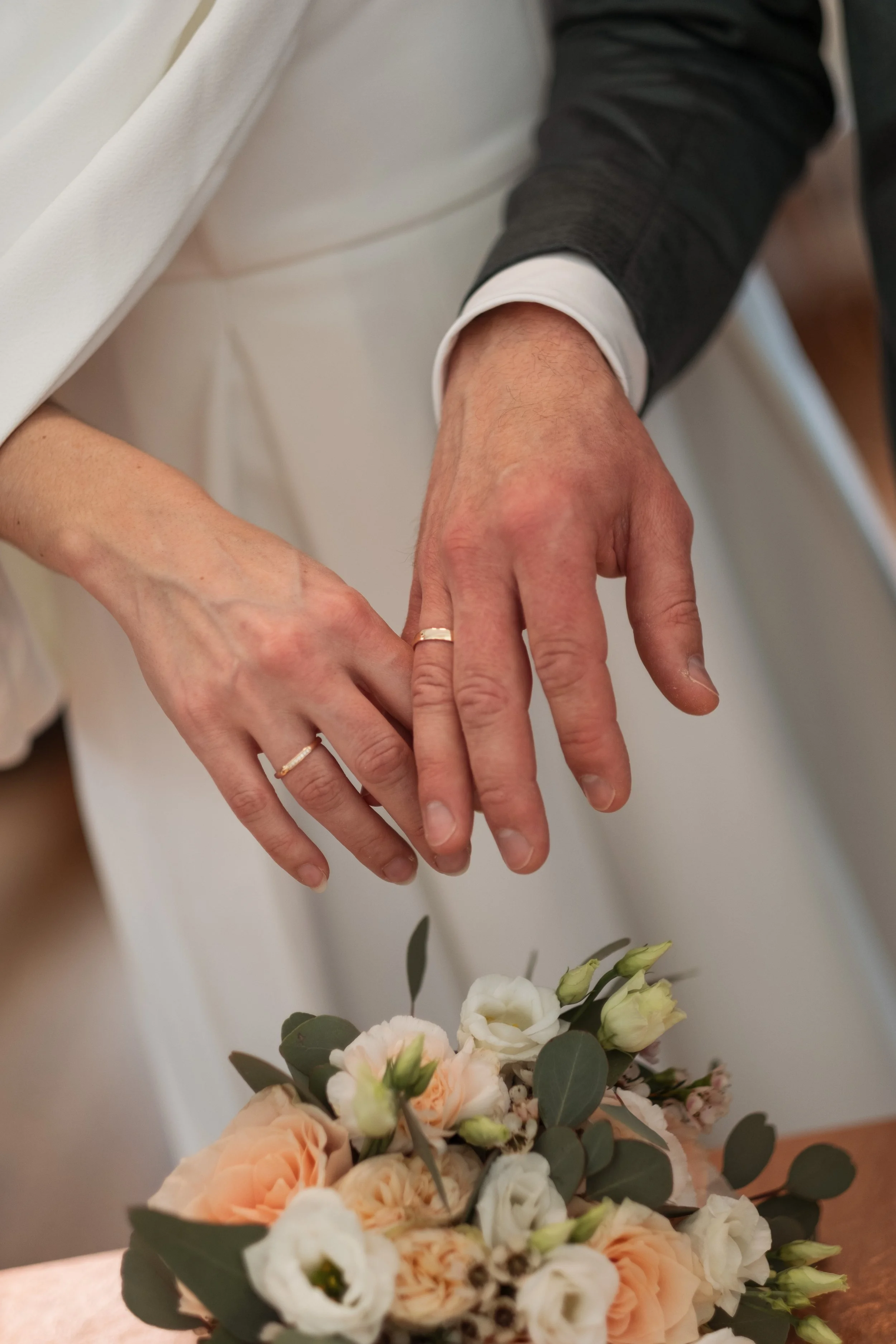 Nahaufnahme der Hände eines Paares, die gemeinsam eine kleine Blumenstrauß halten, mit Eheringen am Ringfinger, bei einer Hochzeitszeremonie.