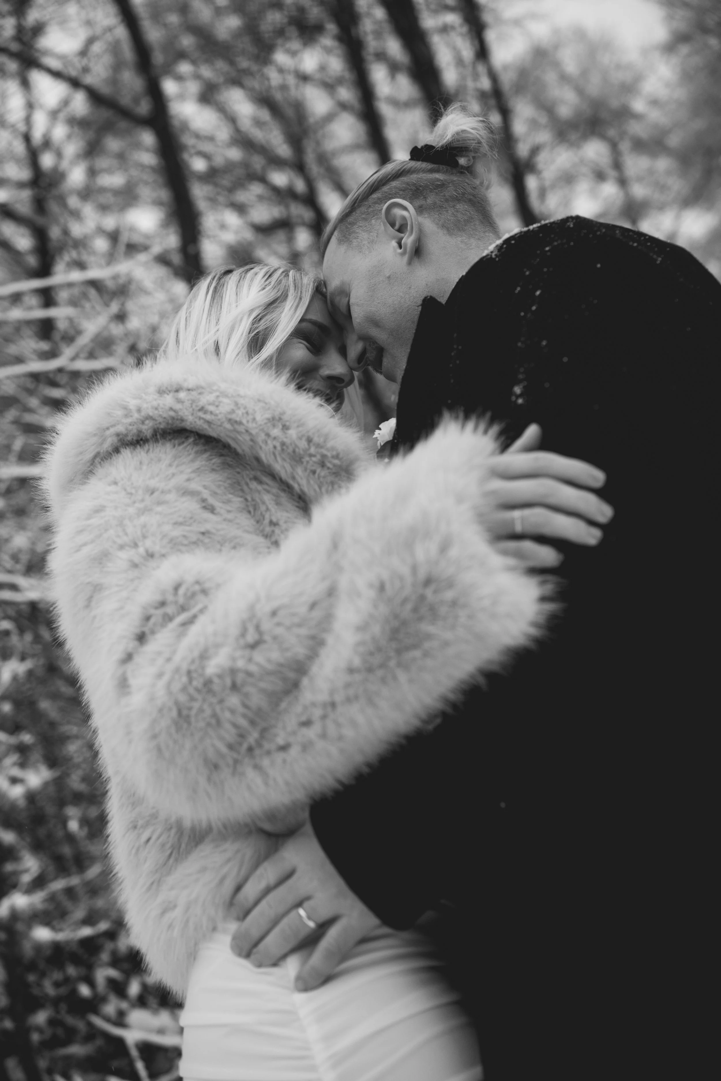 Ein glückliches Paar in Winterkleidung, das sich liebevoll berührt, stehen im Freien mit winterlichen Bäumen im Hintergrund.