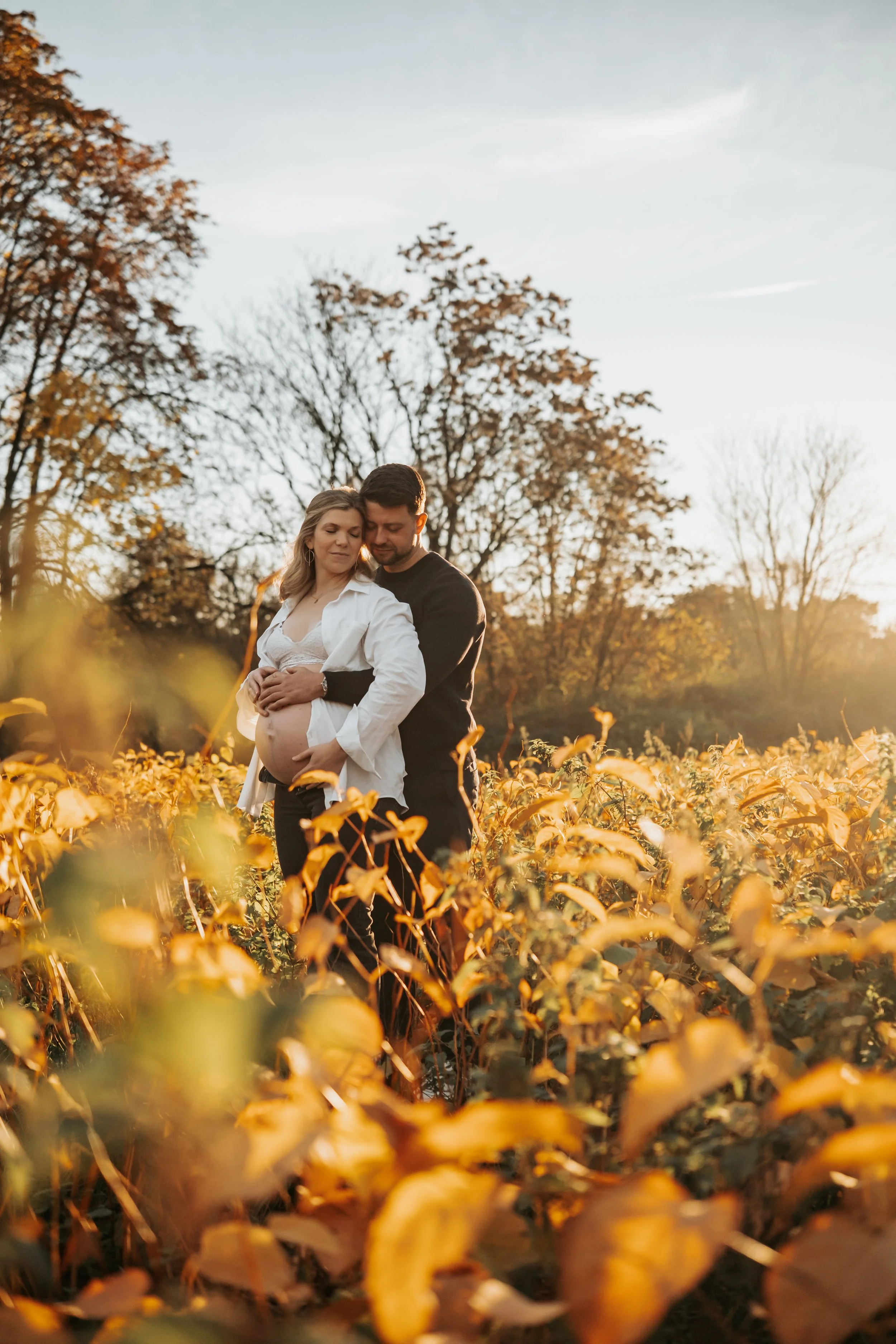 Paare in einem Feld bei Sonnenuntergang, der Mann hält die schwangere Frau.