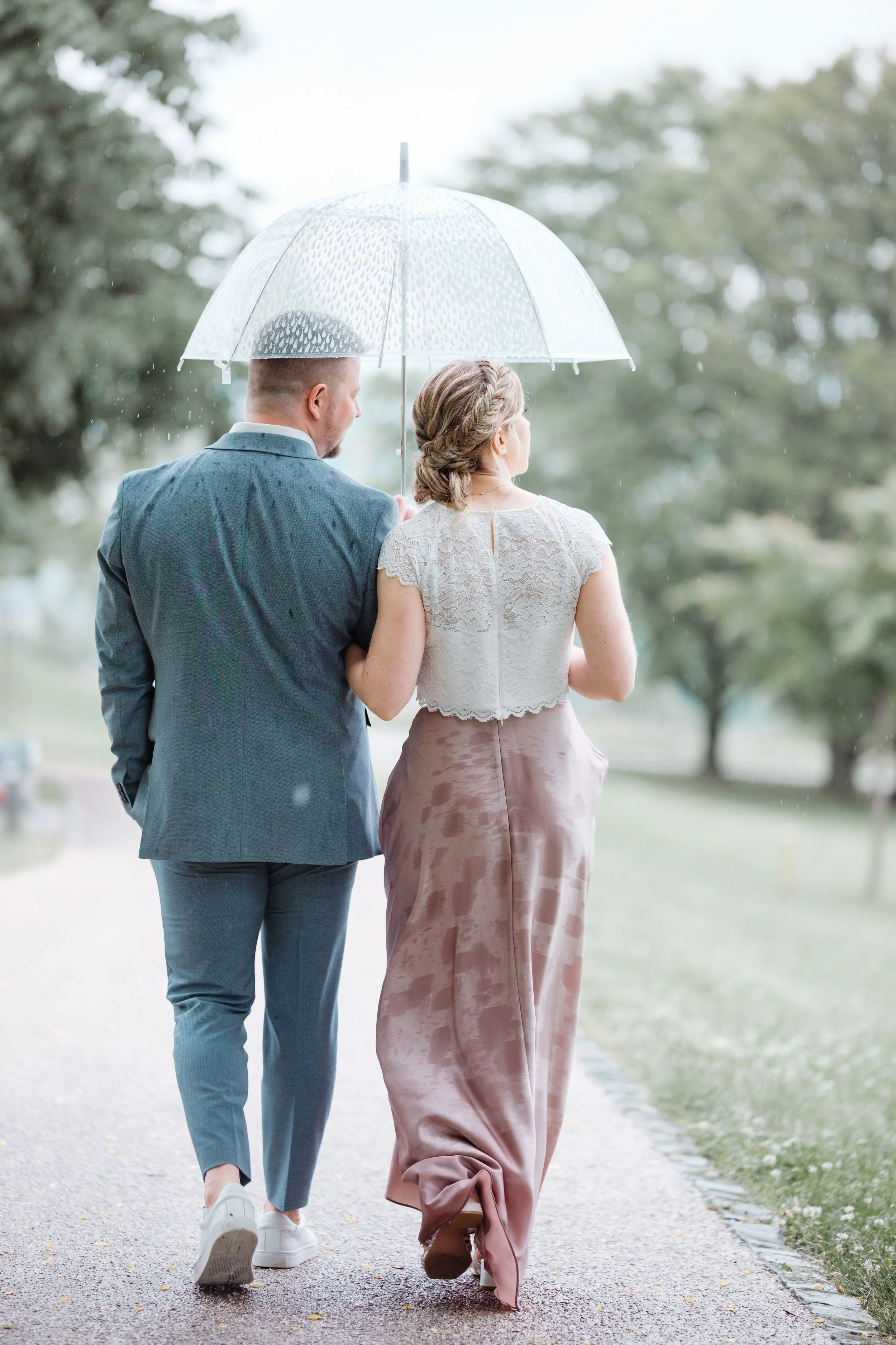 Ein Paar geht Hand in Hand unter einem Regenschirm spazieren, bei Regenwetter im Freien, umgeben von Bäumen