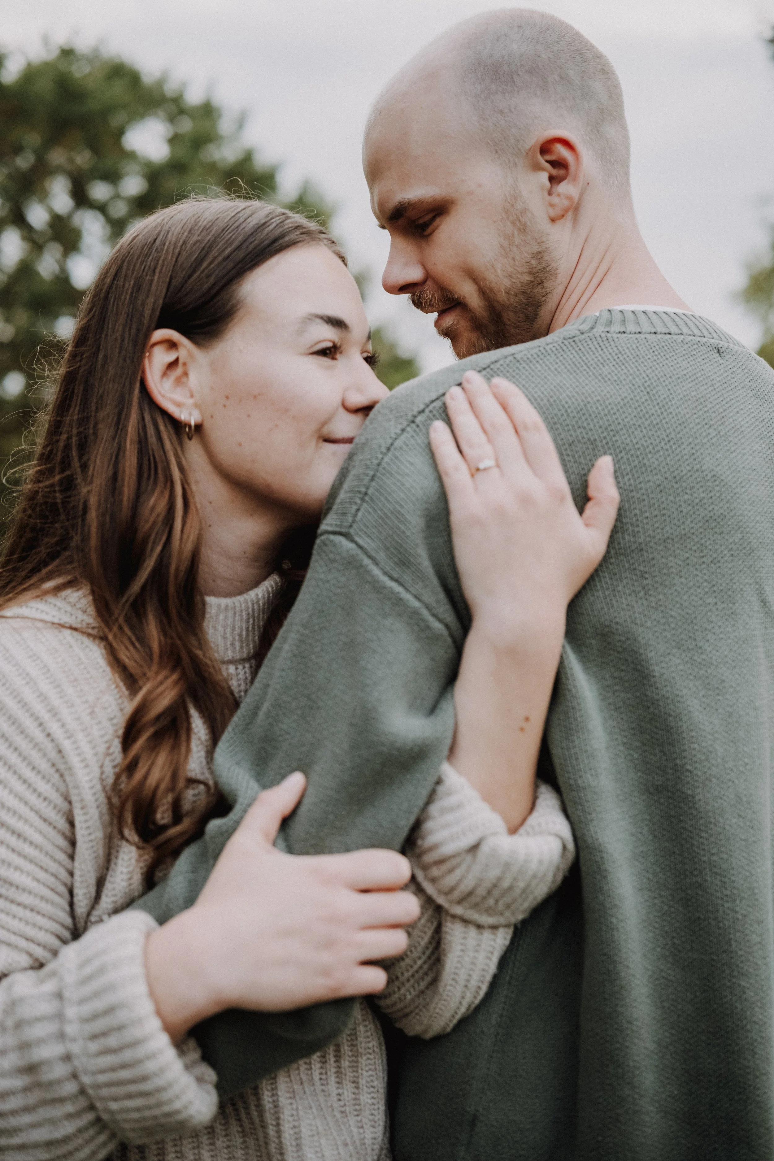 Ein Paar umarmt sich liebevoll im Freien, die Frau trägt einen cremefarbenen Pullover und der Mann einen grünen Pullover.