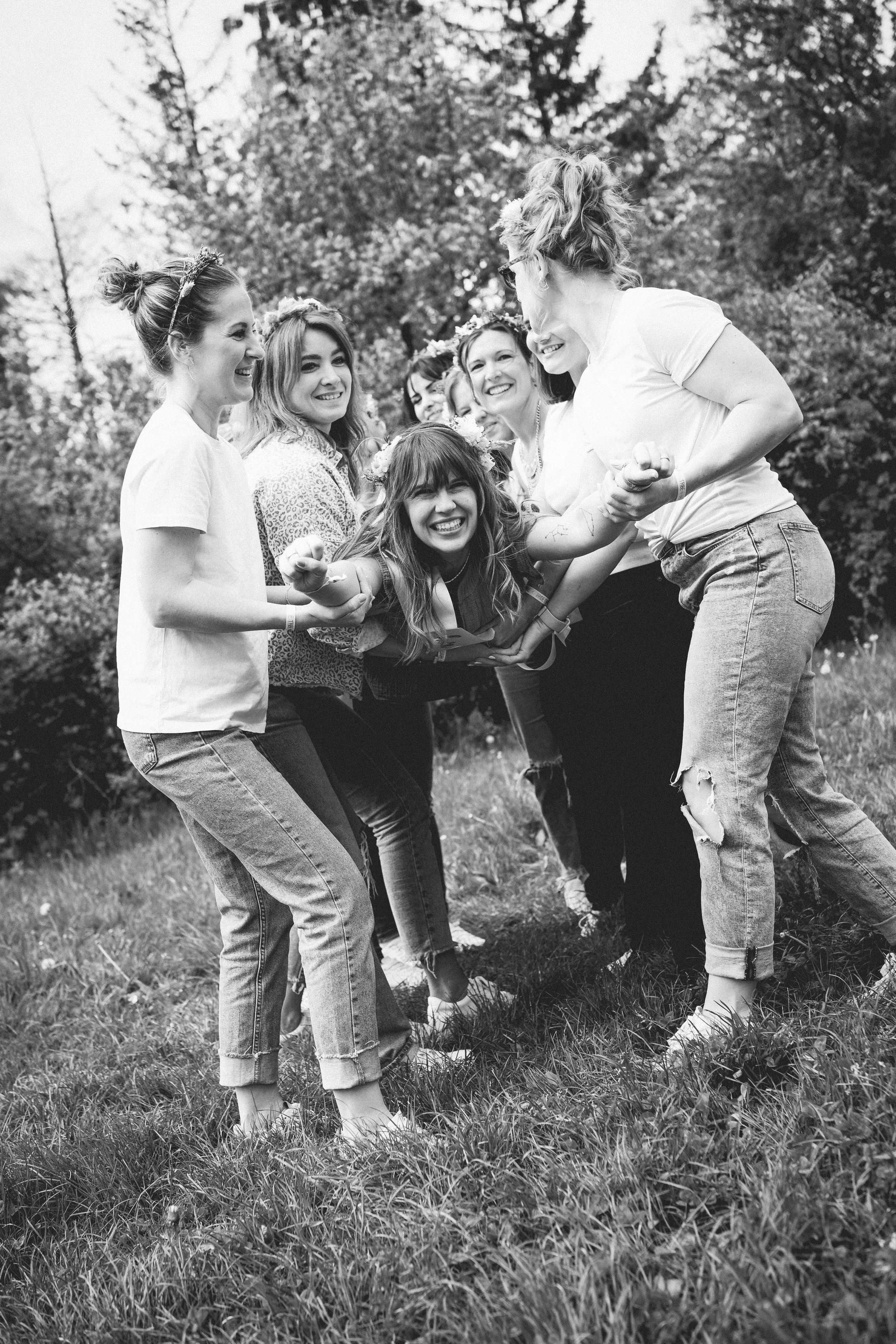 Eine Gruppe von jungen Frauen, die im Freien auf dem Rasen lachen und Spaß haben, umarmt in freundschaftlicher Pose.