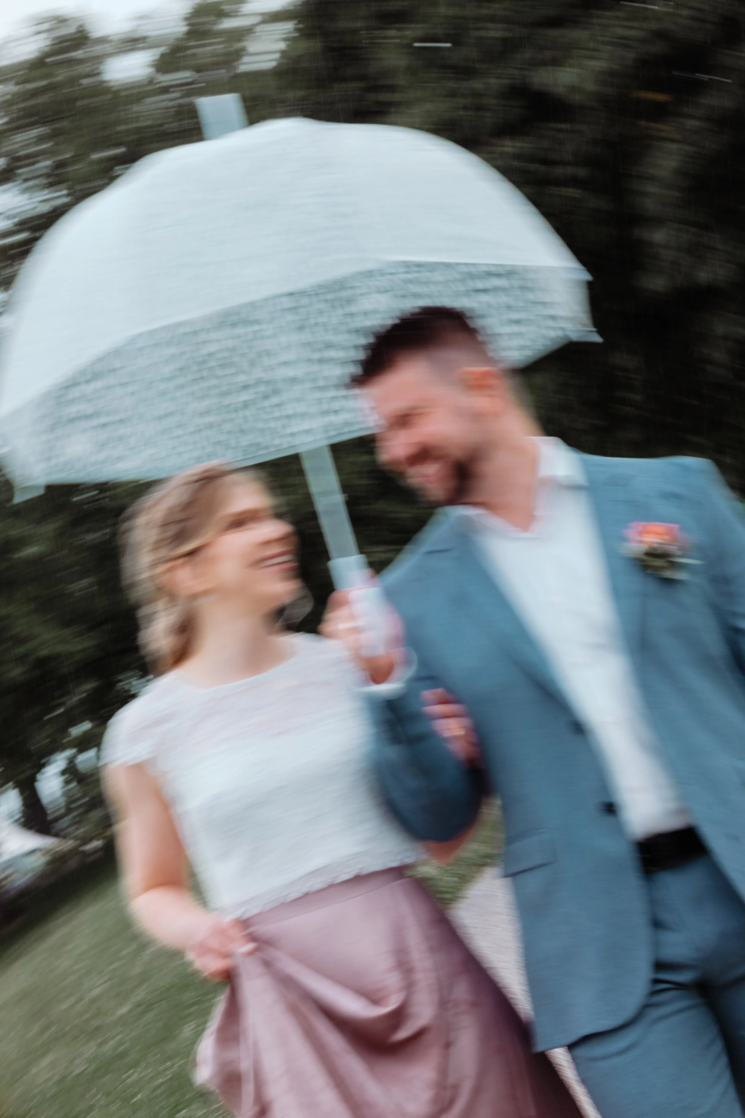 Ein Paar bei einem Hochzeitstag, das unter einem weißen Regenschirm lacht.