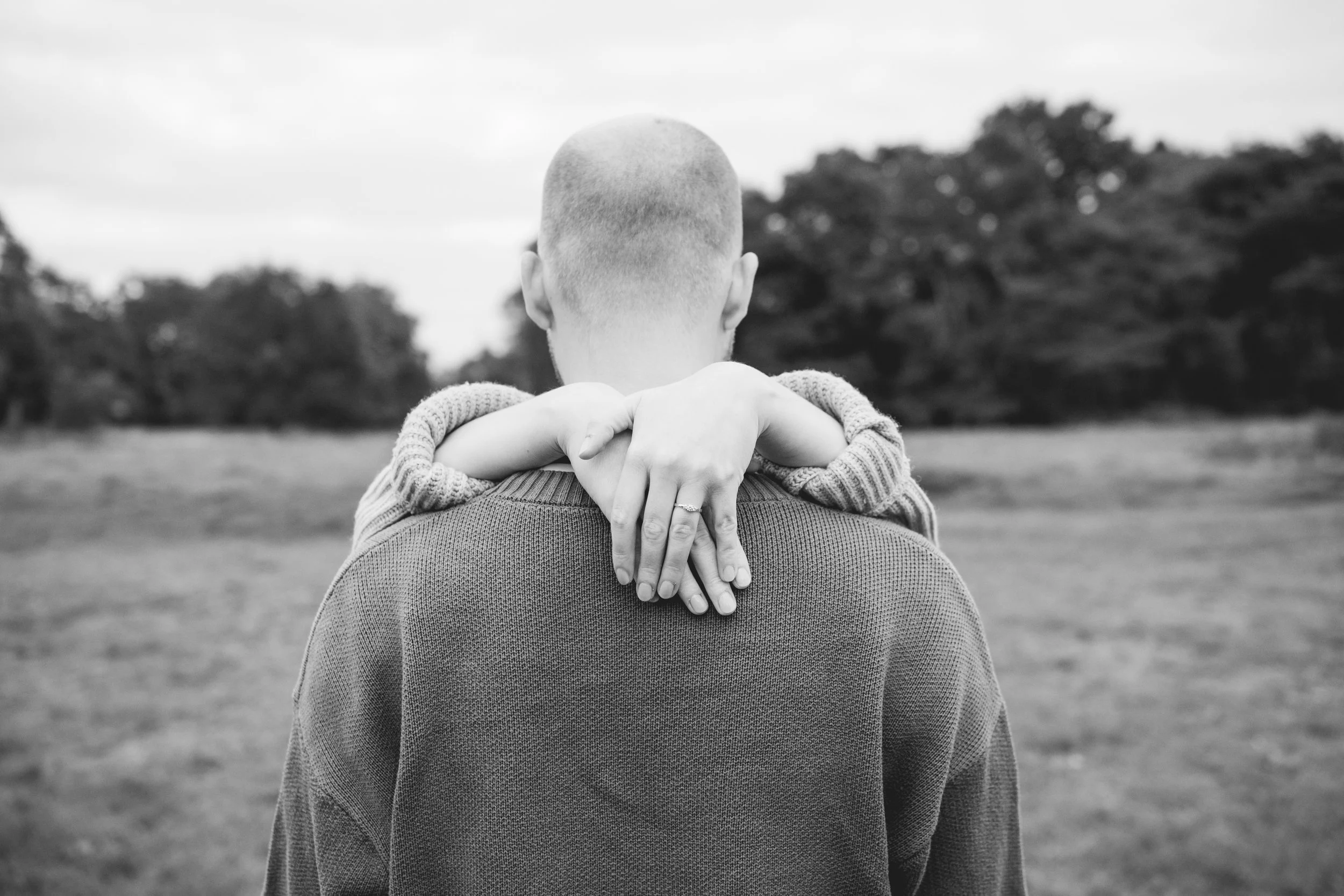 Ein Mann steht im Freien in einem Feld, mit einem Kind, das sich auf seine Schultern setzt und dessen Arme um seinen Hals gelegt hat. Das Bild ist schwarz-weiß.