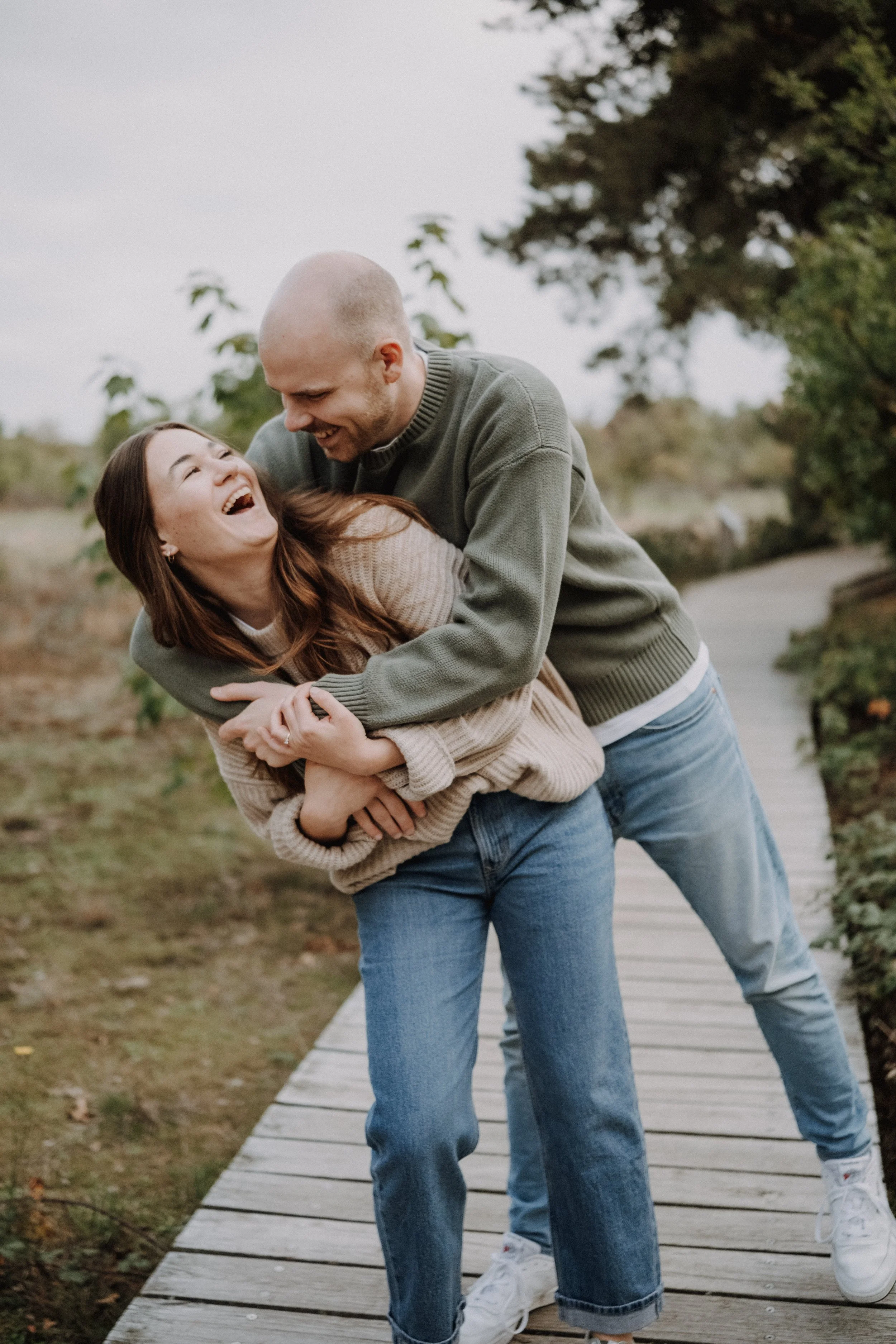 Ein lachendes Paar beim Umarmen auf einem Holzsteg im Freien.