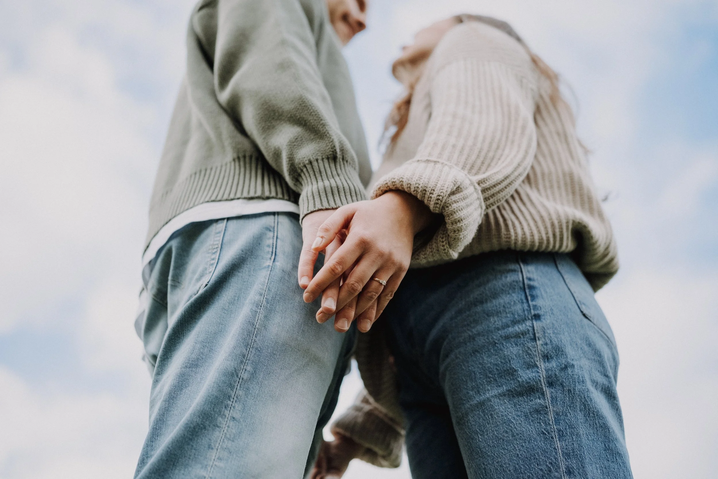 Ein Paar hält sich an den Händen, sichtbar von unten aufgenommen, bei Bewölktem Himmel.