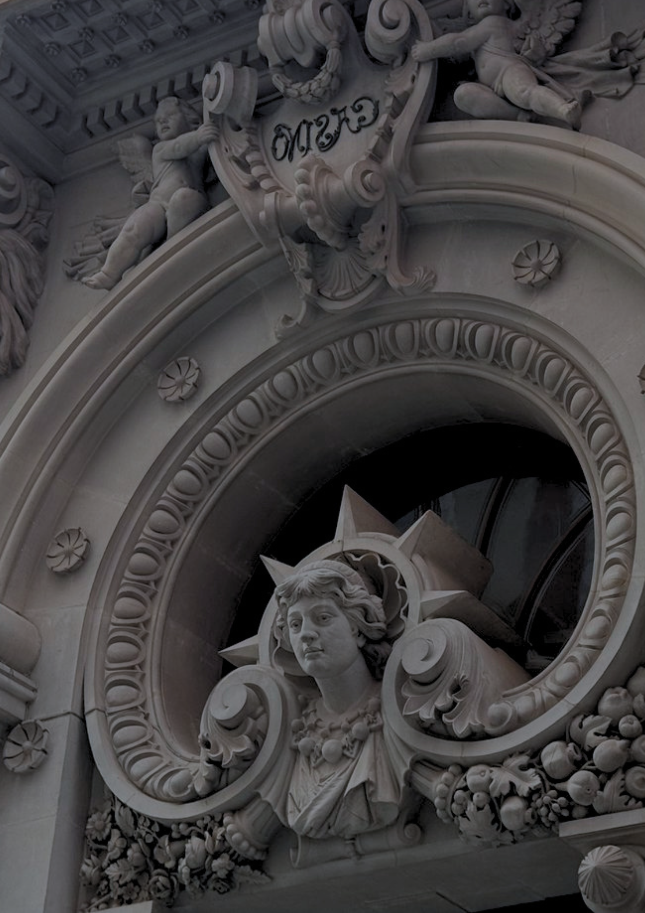 Barocke Fassadendekoration mit einem männlichen Gesicht und der Schrift 'Gute' auf einer weißen Steinskulptur.
