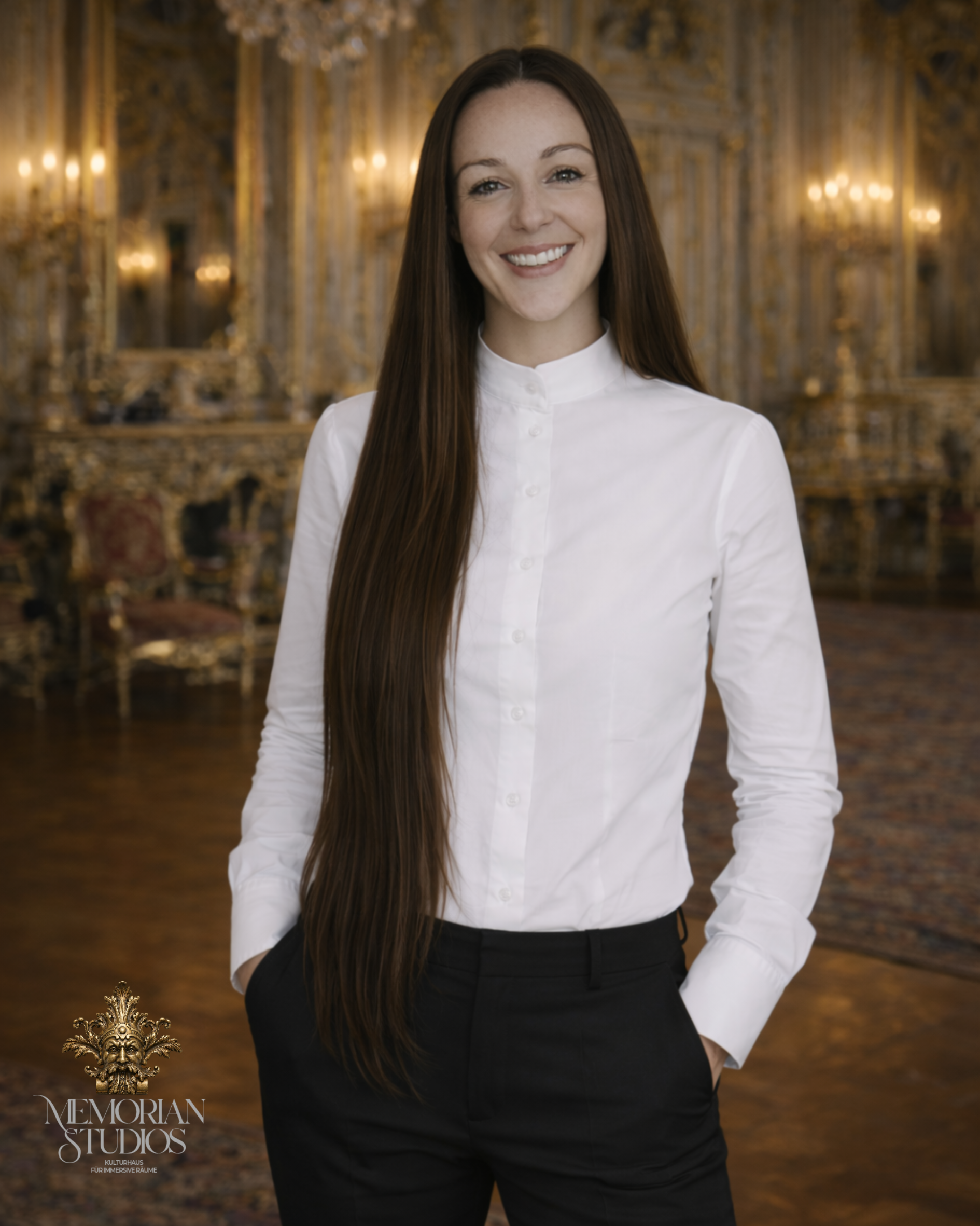 Ein Lächelnder junger Mann steht in einem opulenten, künstlerisch dekorierten Raum mit goldverzierten Wänden. Er trägt eine weiße Hemd-Bluse und schwarze Hosen, seine langen braunen Haare fallen auf die Schultern. Im unteren linken Bereich befindet sich ein Logo und Text, der auf ein Kultur- oder Kunststudio hinweist.