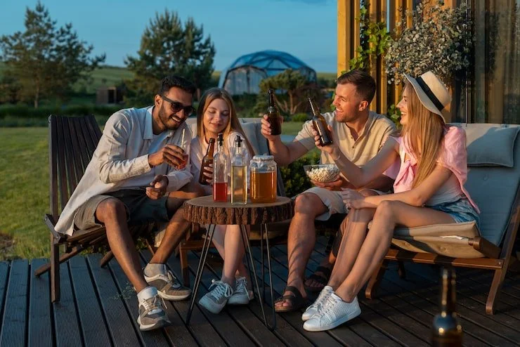Four friends enjoying drinks together outdoors on a wooden deck during sunset.