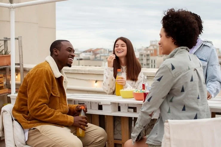 Four friends enjoying drinks and snacks on a rooftop terrace, laughing and talking together.