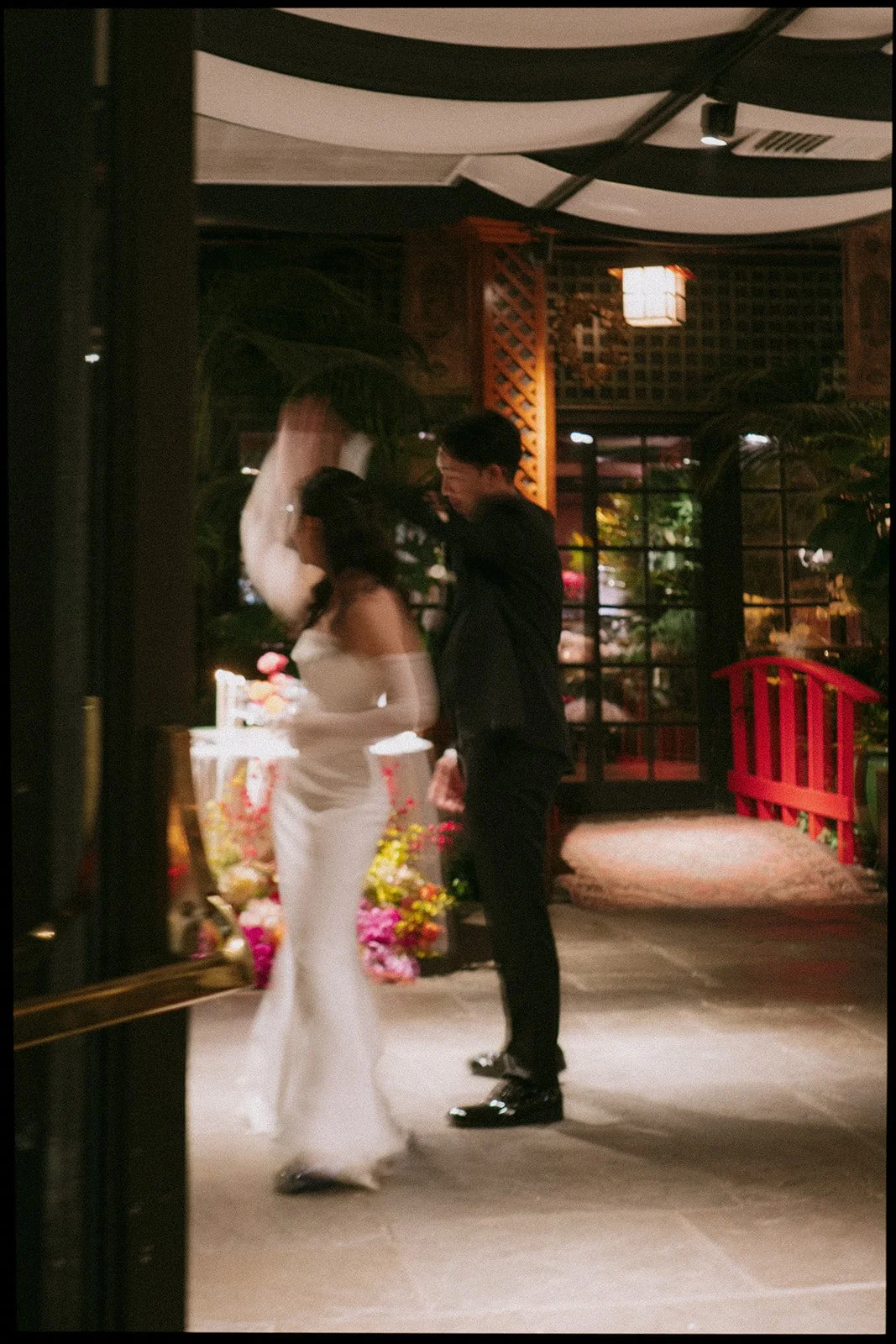 A bride and groom share a dance at their wedding reception in an indoor venue with floral decorations and warm lighting.