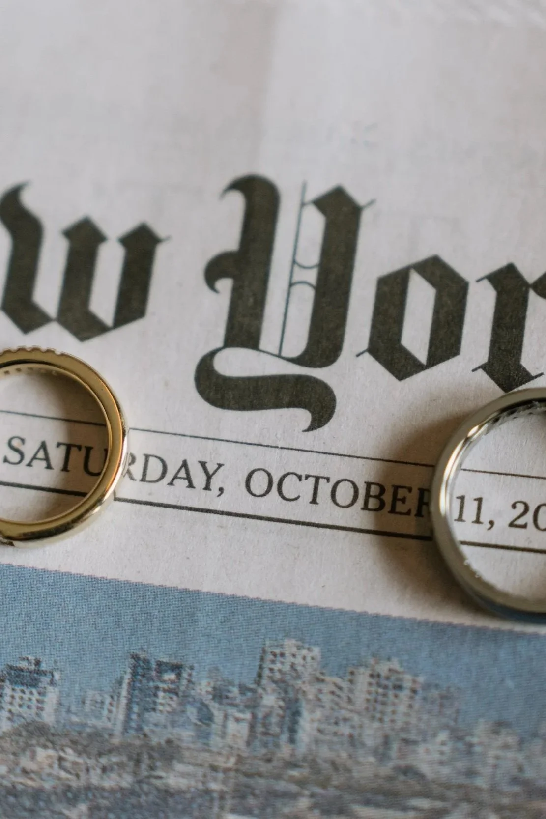 Close-up of two wedding rings placed on a newspaper with the date Saturday, October 11, 2020, and a cityscape image at the bottom.