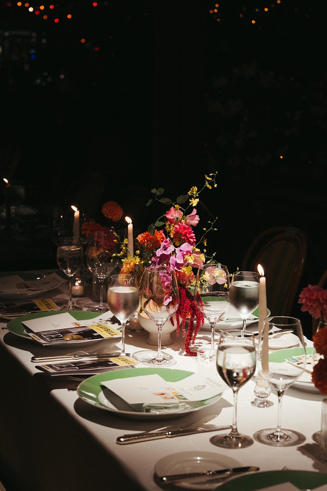 Elegant dinner table set with floral centerpiece, candles, wine glasses, and place settings with menus.