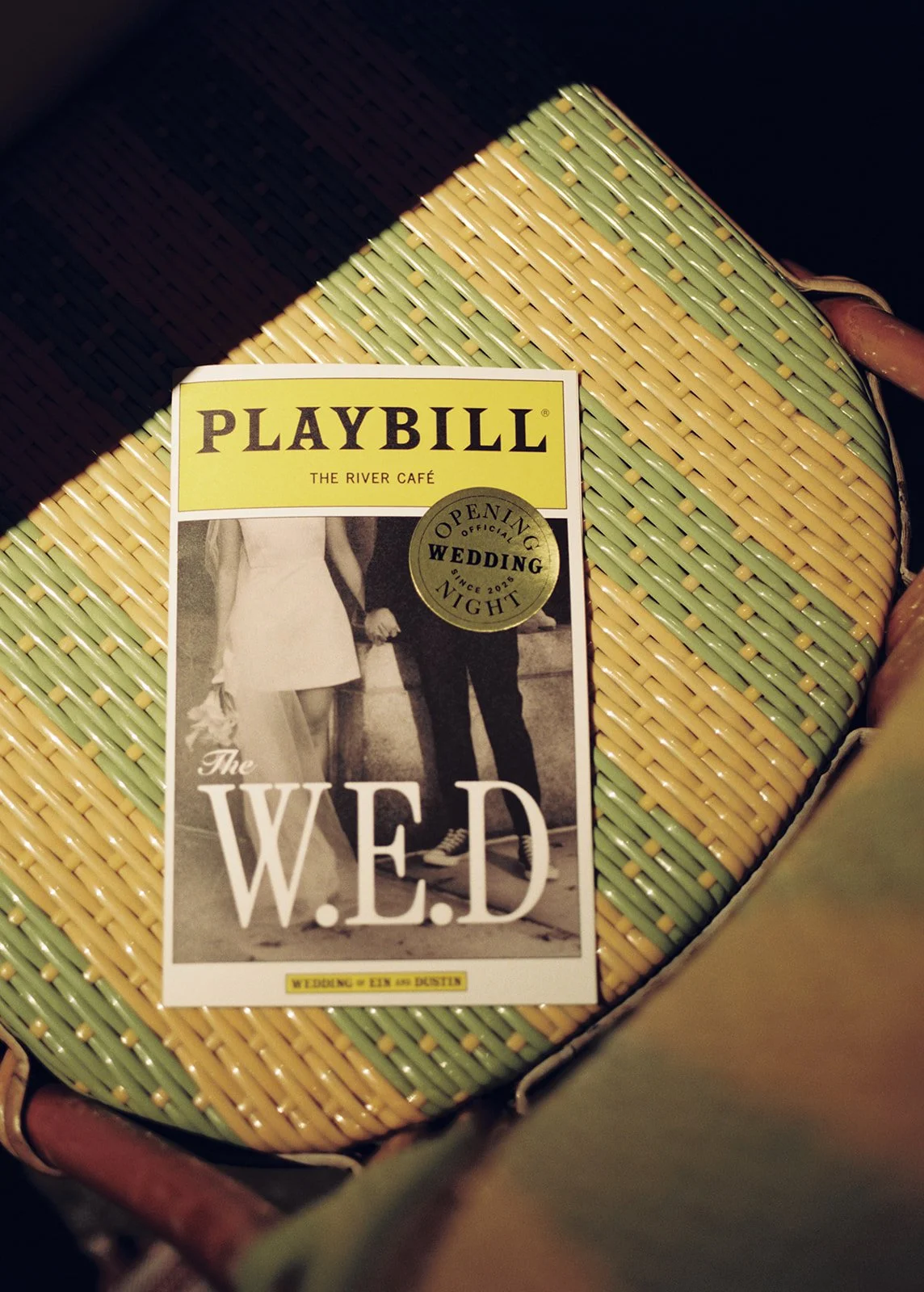 A Playbill theater program for 'The W.E.D.' resting on a woven yellow and green basket or stool.