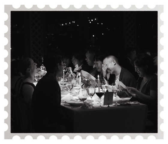 People seated at a dinner table, enjoying a formal event, with wine glasses and table decorations.
