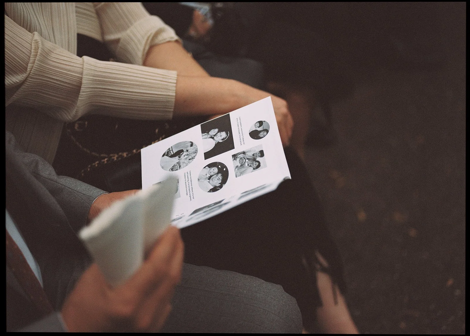 People sitting closely together, one person reading a printed sheet of paper with black and white photos of women, another person holding a tissue.
