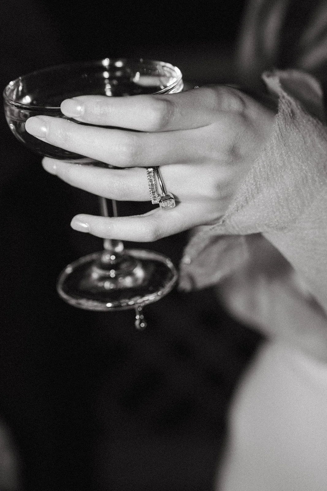 A hand with a ring holding a wine glass in black and white photo.