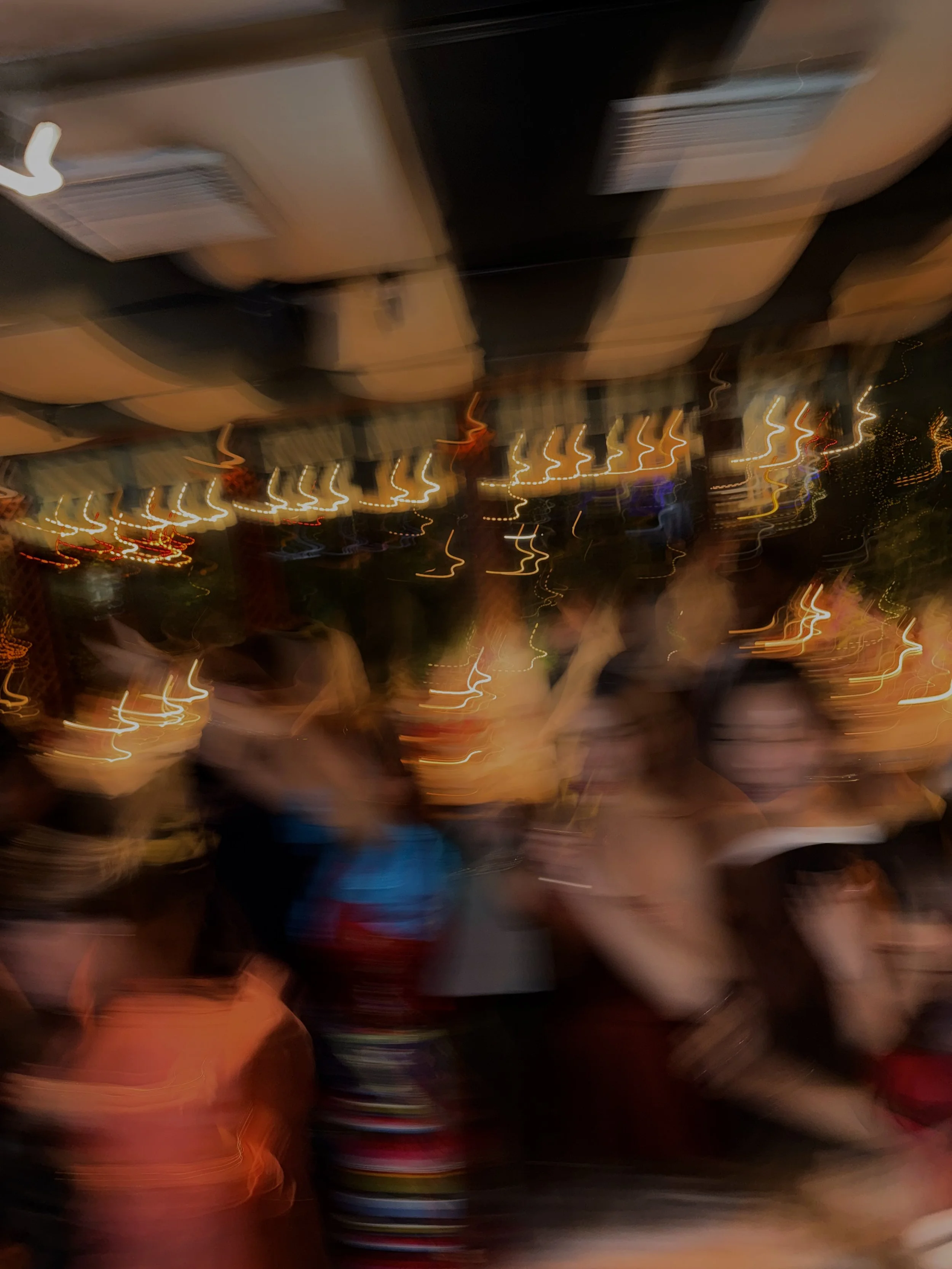 Blurry photo of people at a lively indoor event with warm lighting, some wearing glasses or hats.