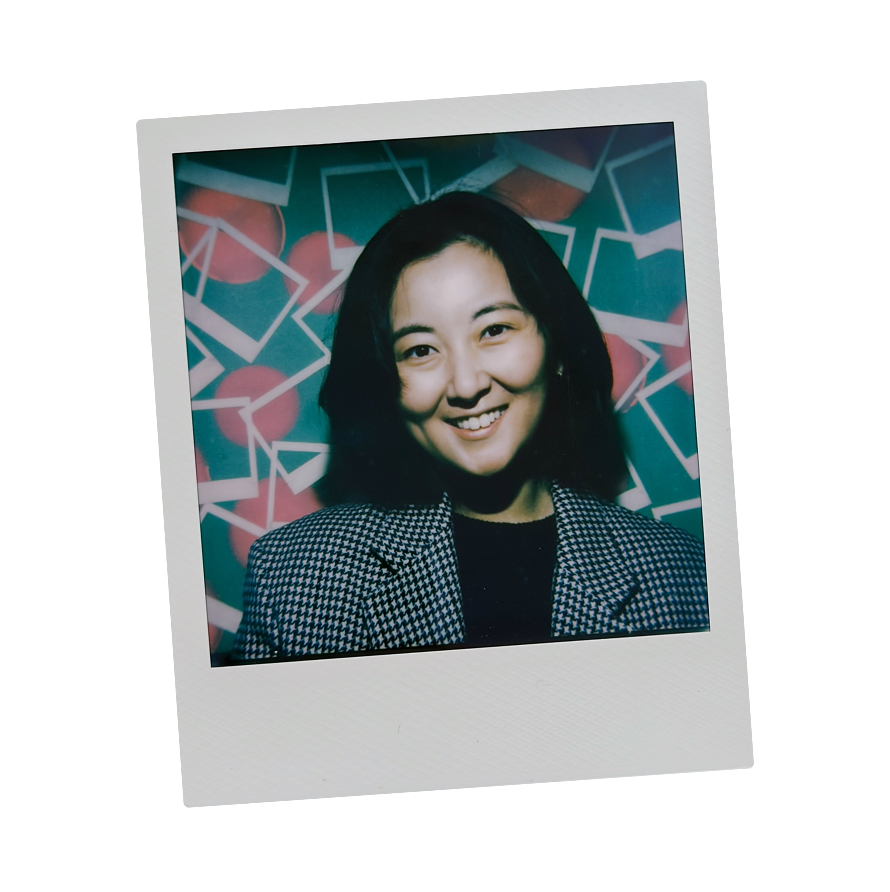 Polaroid photo of a young woman with shoulder-length black hair, smiling, wearing a black and white houndstooth blazer, in front of a colorful geometric background with red circles and white lines.