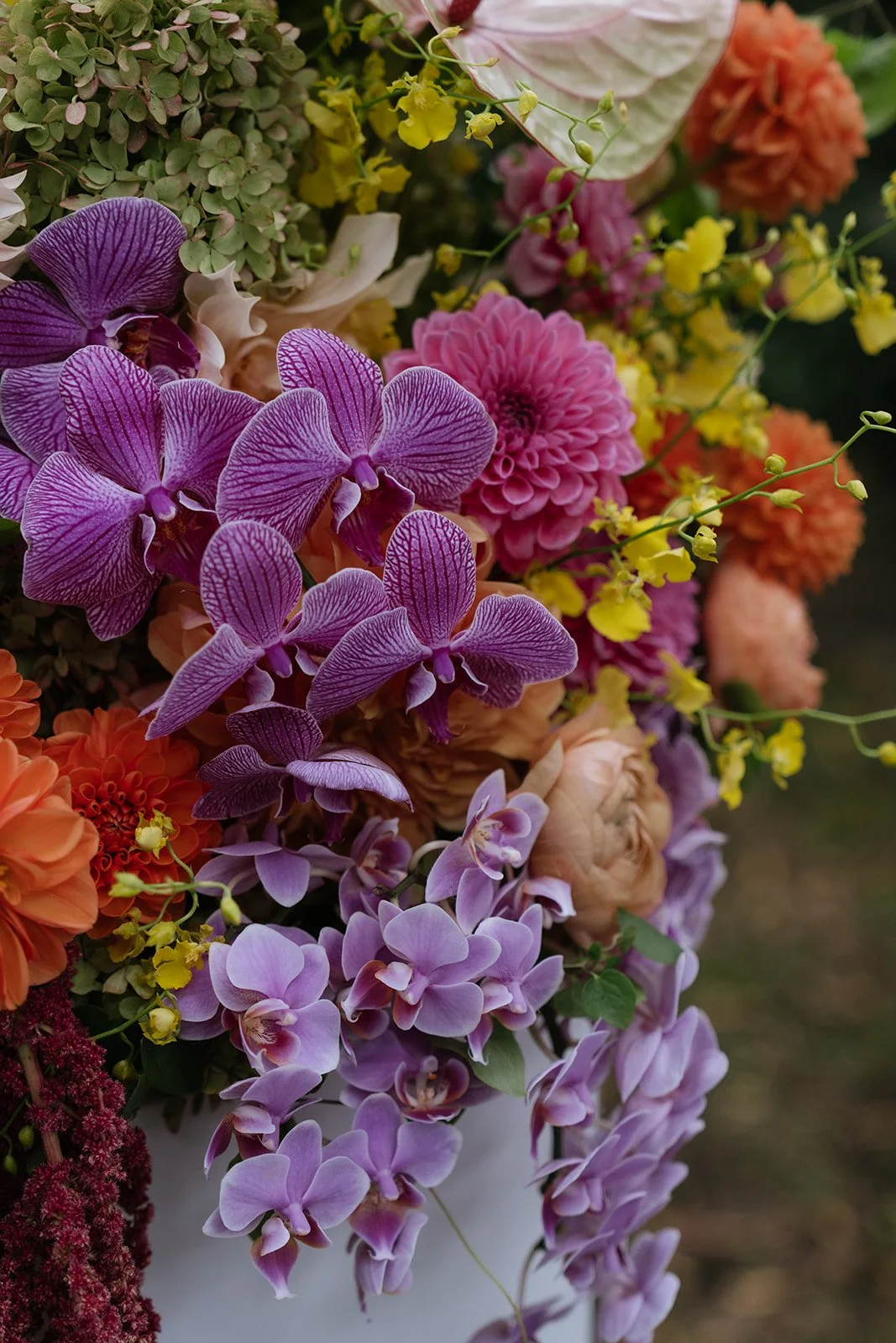 Close-up of a colorful mixed flower bouquet featuring purple orchids, pink dahlias, orange dahlias, and yellow and green accents.