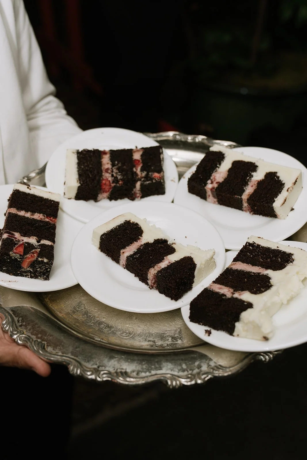 Slices of chocolate cake with pink filling served on white plates, placed on a silver tray.