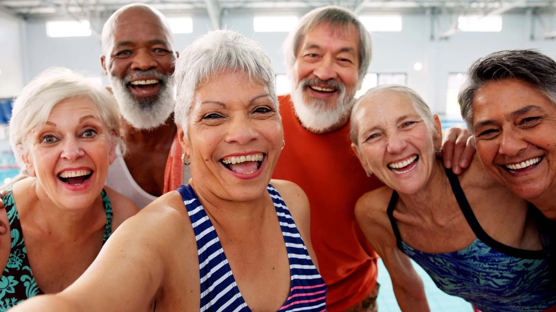 A group of older adults taking a selfie in an indoor swimming pool, smiling and appearing happy.