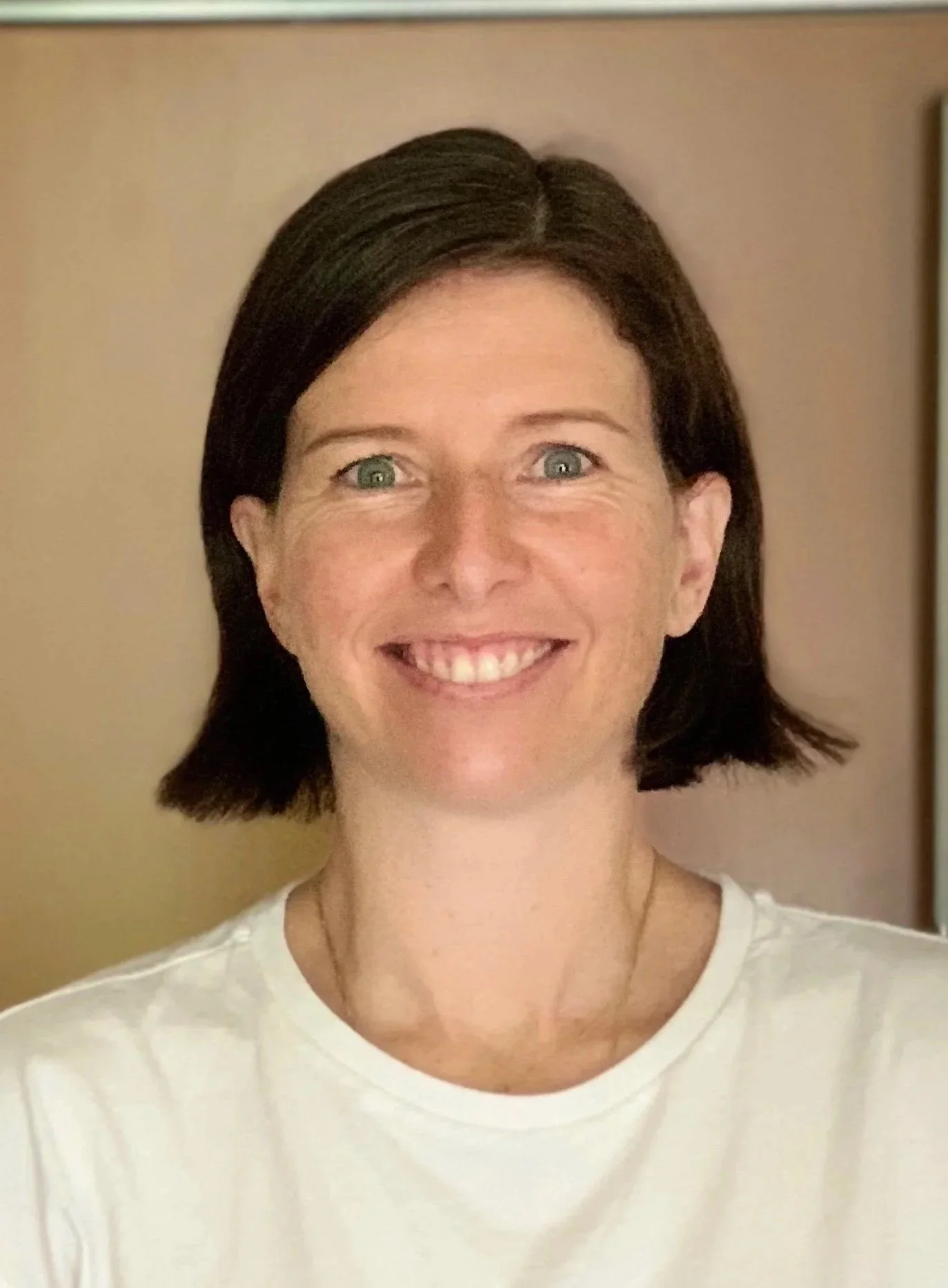 A woman with shoulder-length dark brown hair and blue eyes, smiling slightly, wearing a red shirt, standing against a plain light-colored wall.